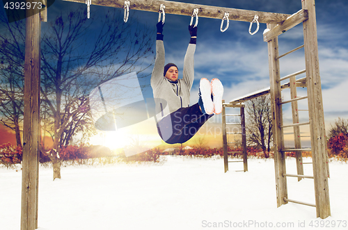 Image of young man exercising on horizontal bar in winter