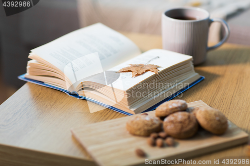 Image of book with autumn leaf, cookies and tea on table