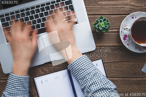 Image of Man working on laptop placed on wooden desk