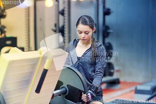 Image of young woman adjusting leg press machine in gym