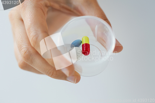 Image of close up of female hand with pills in medicine cup