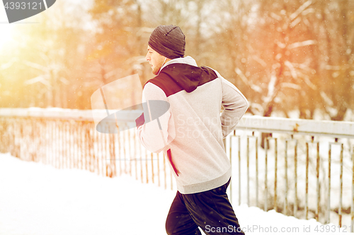 Image of man in earphones running along winter bridge