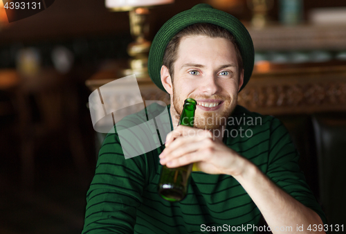 Image of man drinking beer from green bottle at bar or pub