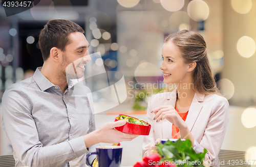 Image of happy couple with present and flowers in mall