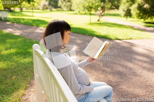 Image of happy pregnant asian woman reading book at park