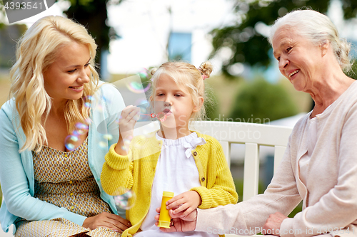 Image of happy family blowing soap bubbles at park