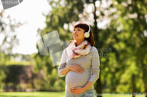 Image of happy pregnant asian woman in headphones at park