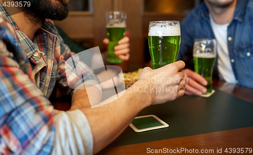 Image of male friends drinking green beer at bar or pub