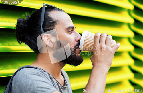 Image of man drinking coffee from paper cup over wall