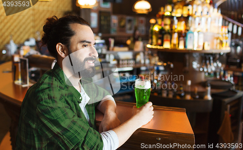 Image of man drinking green beer at bar or pub