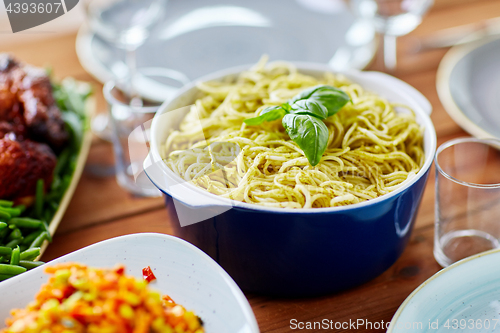 Image of pasta with basil in bowl and other food on table