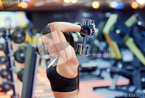 Image of young woman flexing muscles with dumbbell in gym