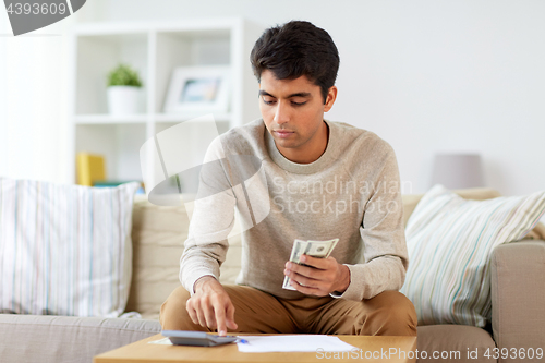 Image of man with calculator counting money at home