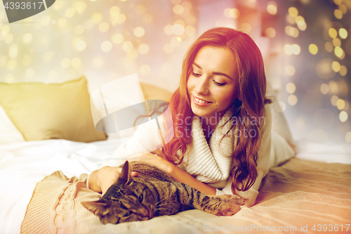 Image of happy young woman with cat lying in bed at home