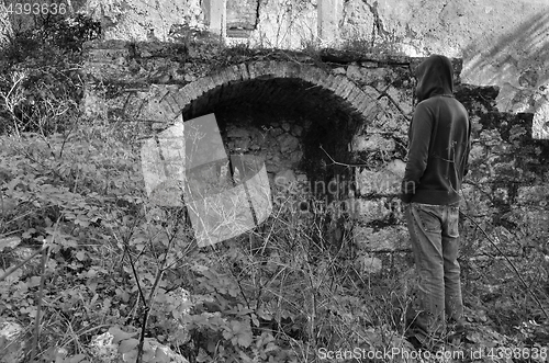 Image of hooded man next to arched recess of rural ruin