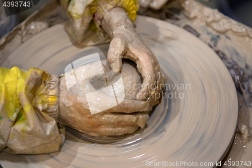 Image of Hands of young girl in process of making clay bowl on pottery wh