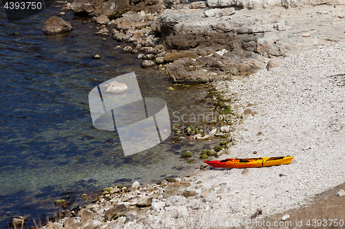 Image of Orange kayak on pebbly beach of sea coast at sun summer day