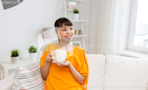 Image of happy asian woman drinking tea or coffee at home
