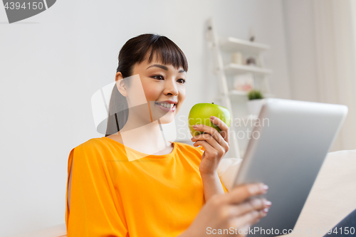 Image of happy asian woman with tablet pc and apple at home