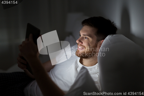Image of young man with tablet pc in bed at home bedroom