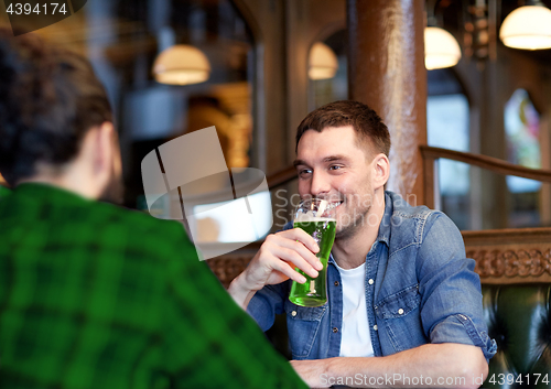 Image of male friends drinking green beer at bar or pub