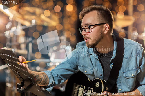 Image of man with guitar writing to music book at studio