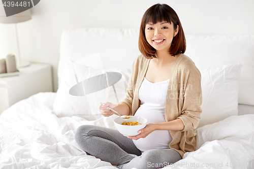 Image of happy pregnant woman eating cereal flakes at home