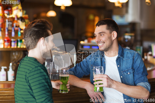 Image of male friends drinking green beer at bar or pub