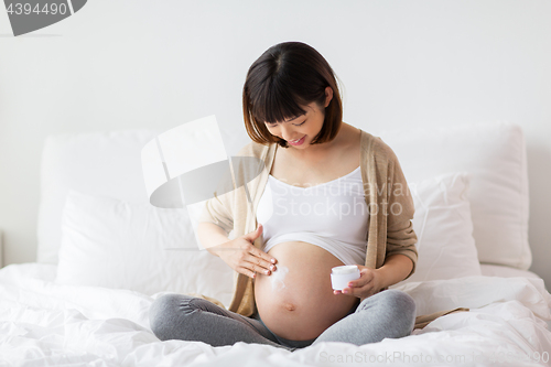 Image of happy asian pregnant woman applying cream to belly