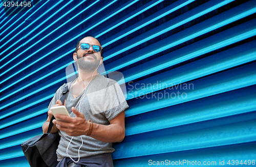 Image of man with earphones and smartphone over wall