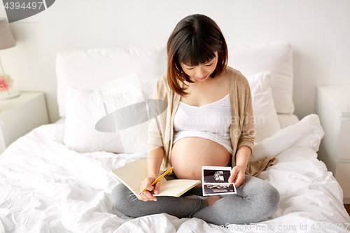 Image of pregnant woman with fetal ultrasound image at home