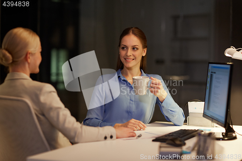 Image of businesswomen drinking coffee at night office