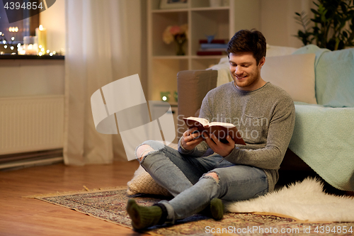 Image of happy young man reading book at home