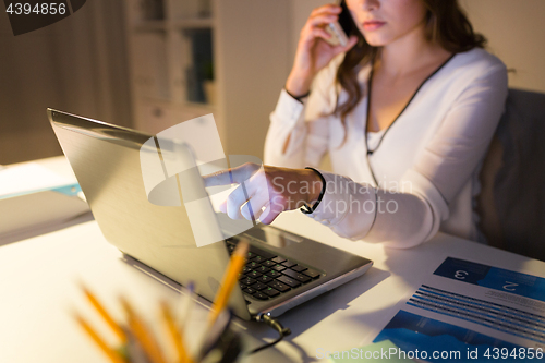 Image of woman with laptop calling on smartphone at office