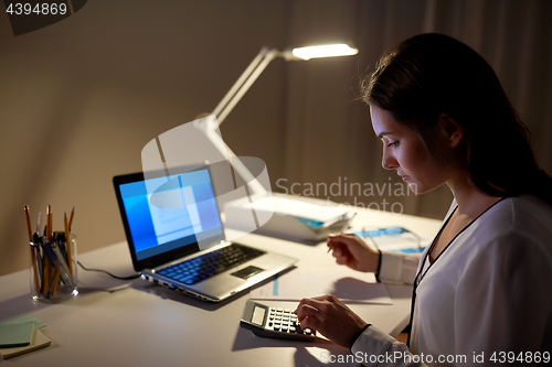 Image of woman with calculator and papers at night office