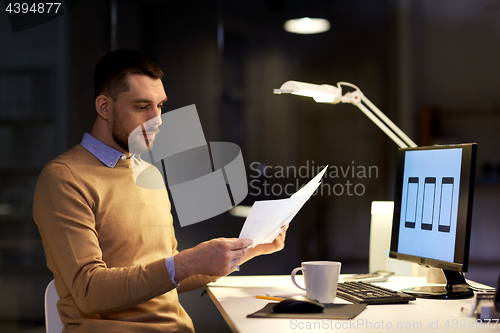 Image of man with papers and computer works at night office
