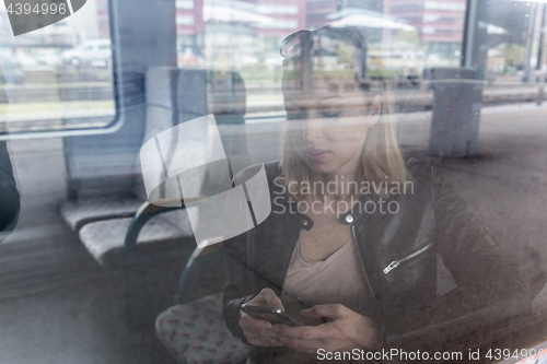 Image of Young woman traveling by train, using smart phone.