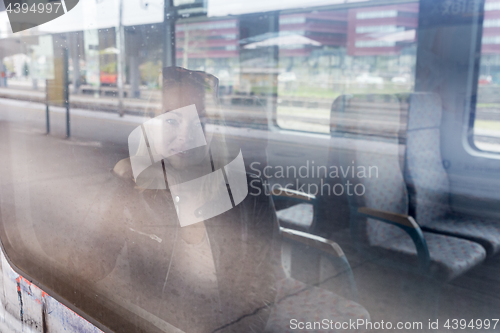 Image of Young woman traveling by train, looking out window while sitting in train.