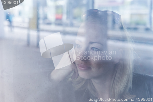 Image of Young woman traveling by train, looking out window while sitting in train.