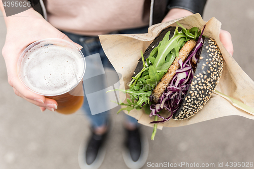 Image of Female Hands Holding Delicious Organic Salmon Vegetarian Burger and Homebrewed IPA Beer.