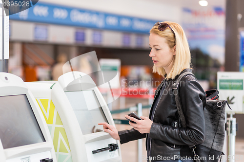 Image of Casual caucasian woman using smart phone application and check-in machine at the airport getting the boarding pass.