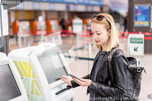 Image of Casual caucasian woman using smart phone application and check-in machine at the airport getting the boarding pass.