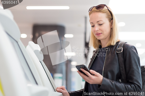 Image of Casual caucasian woman using smart phone application and check-in machine at the airport getting the boarding pass.