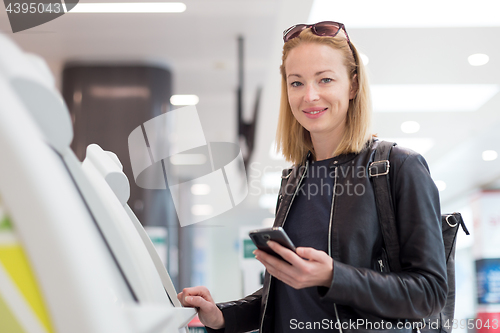 Image of Casual caucasian woman using smart phone application and check-in machine at the airport getting the boarding pass.