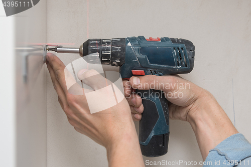 Image of The master screws the furniture corner to the cabinet with a screwdriver, close-up