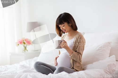 Image of happy pregnant woman with cup drinking tea at home