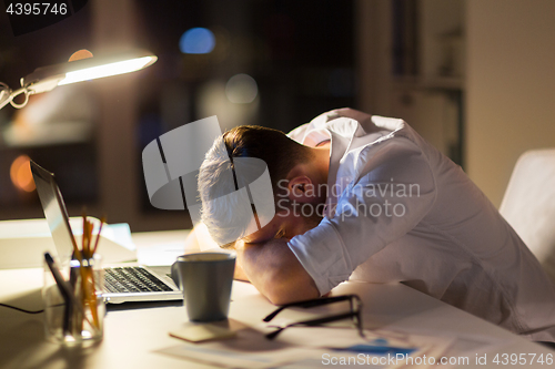 Image of tired businessman lying on table at night office