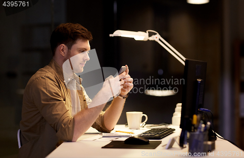 Image of man with smartphone working late at night office