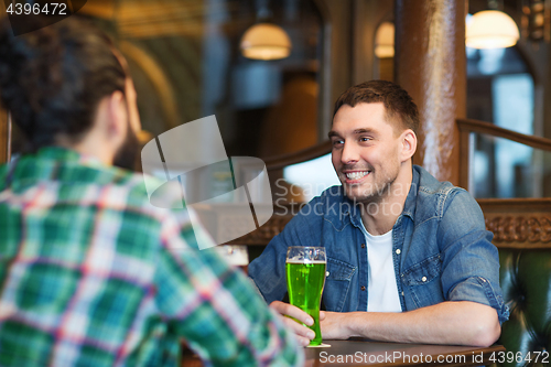 Image of male friends drinking green beer at bar or pub