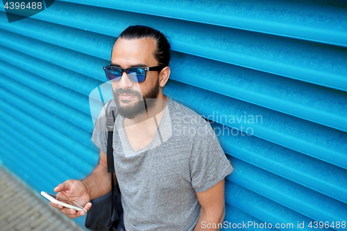 Image of man in sunglasses with smartphone and bag at wall
